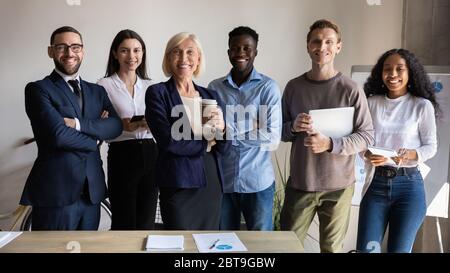 Sorridendo dipendenti diversi che si pongono insieme per un ritratto aziendale in ufficio Foto Stock