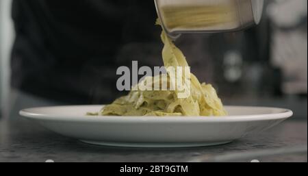 l'uomo ha messo il pesto fettuccine nel recipiente della pasta sul piano di cemento Foto Stock