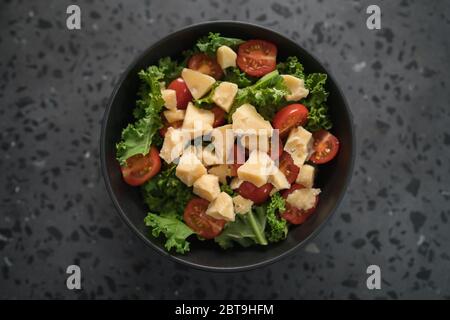 Insalata con pomodori ciliegini, kale e formaggio in ciotola nera su fondo di cemento Foto Stock