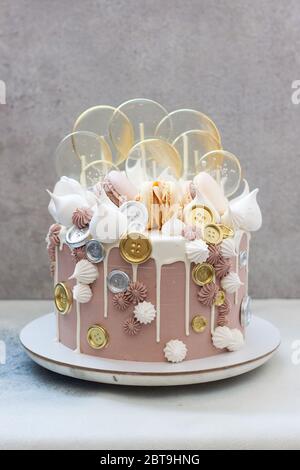 Torta di birhtday di colore marrone chiaro e dorato con macaroon, monete, meringa e lecca su sfondo grigio. Foto Stock