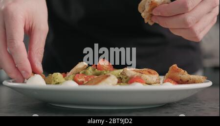 l'uomo ha messo le fette di pollo sulle fettuccine del pesto con mozzarella e. pomodori ciliegini nel recipiente per la pasta sul piano di cemento Foto Stock