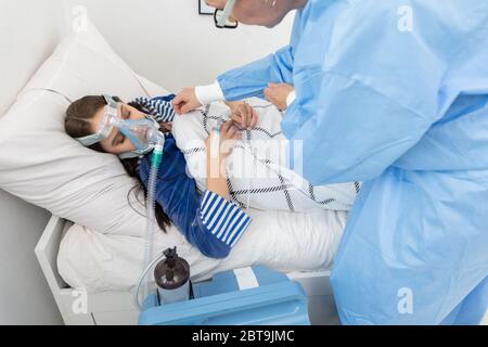 Il medico controlla il collegamento del ventilatore. L'adolescente si trova su un letto d'ospedale. Maschera di ossigeno sul tratto respiratorio. Foto Stock