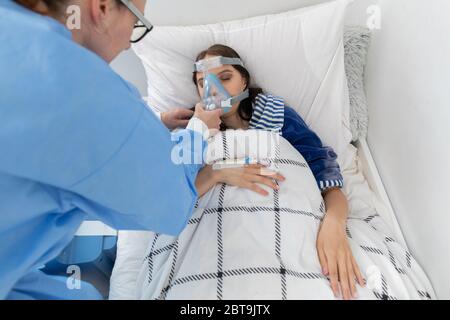 Il medico controlla il collegamento del ventilatore. L'adolescente si trova su un letto d'ospedale. Maschera di ossigeno sul tratto respiratorio. Foto Stock