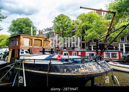 Vecchia nave arrugginita e una casa galleggiante ormeggiata lungo un canale ad Amsterdam, Paesi Bassi Foto Stock