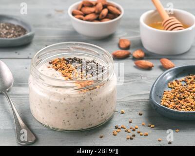 Per una notte di avena in vaso e ingredienti - semi di Chia, mandorla, miele e polline in legno grigio sfondo tabella. Sana colazione fiocchi d'avena ricetta idea Foto Stock