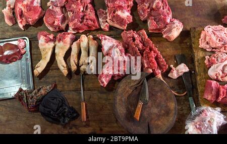 assortimento di carne cruda e coltello sul tavolo di lavoro in legno scuro del macellaio. Vista dall'alto. Foto Stock