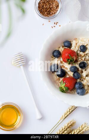 Porridge di farina d'avena con fragola, mirtillo, semi di lino e miele su sfondo bianco. Colazione sana per bambini e genitori. Cibo vegetariano. Foto Stock