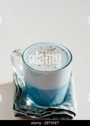 Latte di pea blu o latte di matcha blu con spazio per la copia. Latte fresco caldo con fiori di pisello blu a farfalla o latte clitoria ternatea in tazza di vetro al tramonto naturale luce dura. Sfondo bianco. Verticale Foto Stock