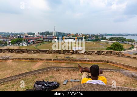 Un appassionato di sport guarda il cricket che si gioca al Galle International Stadium dai bastioni della città. Foto Stock