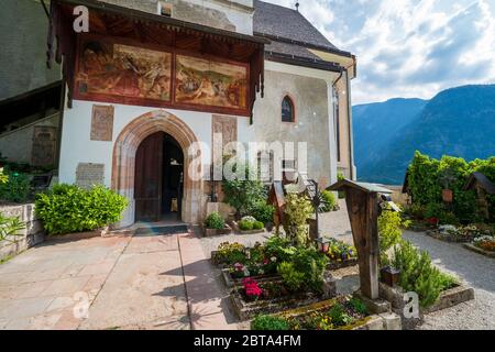 Il cimitero che circonda la Chiesa Parrocchiale di Hallstatt, Salzkammergut, OÖ, Austria, e un bellissimo affresco sopra l'ingresso della chiesa Foto Stock