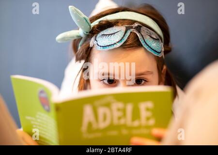 Ragazza giovane che indossa una maschera e che legge un fumetto francese (Mortelle Adèle) Foto Stock