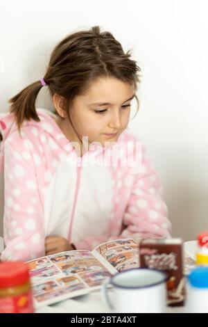 Giovane ragazza che legge un fumetto a colazione Foto Stock