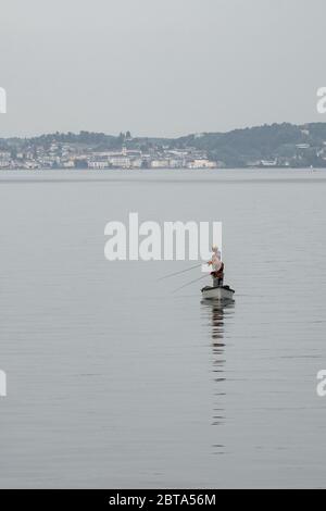 Due uomini che si trovano su una barca da pesca e cercano di pescare nel lago Traunsee, regione del Salzkammergut, Austria, città di Gmunden sullo sfondo Foto Stock