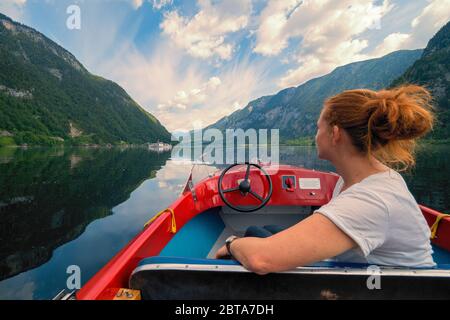 Crociera turistica femminile con piccola barca rossa sul lago Hallstatt di fronte allo splendido paesaggio montano vicino Hallstatt, regione Salzkammergut, OÖ, Austria Foto Stock