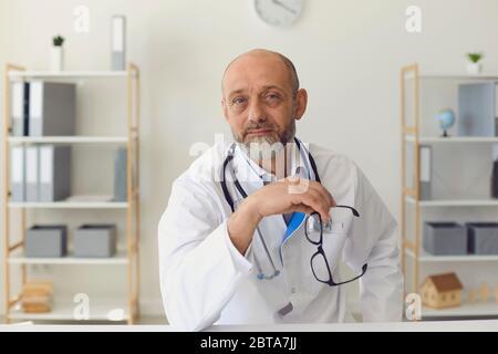 Un medico di mezza età sta guardando la fotocamera. Medico maturo con una barba grigia lavora comunica con un cliente in clinica. Servizio medico. Foto Stock
