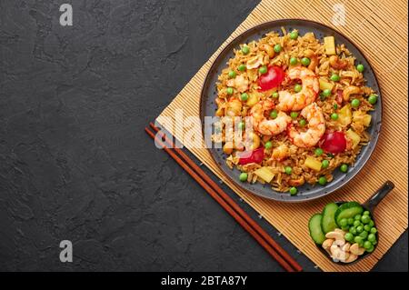 Riso fritto di ananas tailandese o Kao Pad Sapparod su un piatto nero su sfondo di ardesia scuro. Il Kao Pad Sapparod è un piatto di cucina thailandese con riso, gamberi, spilla Foto Stock