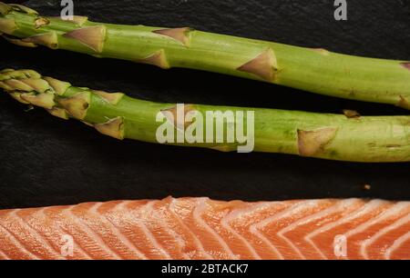 Salmone Pesce cucina Filetto Raw Pepe sale olio di oliva Rosmarino limone Verde Asparagi Tavola di legno Lifestyle concetto sano. Foto Stock