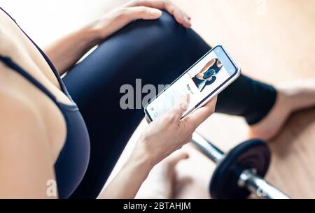 App di allenamento sul telefono cellulare. Allenamento domestico donna in forma. Motivazione della palestra da personal trainer online. Persona che guarda il video tutorial con lo smartphone. Foto Stock