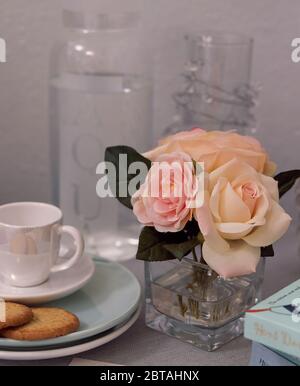 Rose rosa in vaso di vetro sul tavolo accanto a tazza + piatto Foto Stock