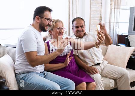 Il marito, la moglie e il figlio turchi con gli occhiali celebrano il Ramadan Festival dei loro parenti tramite videochiamata su uno smartphone. Foto Stock