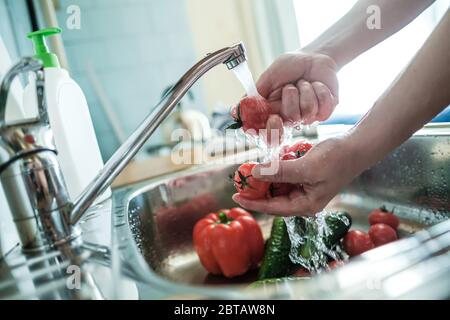 Le mani femminili lavano i pomodori rossi sotto un flusso d'acqua, sullo sfondo delle verdure nel lavandino. Cucina cibo. Foto Stock