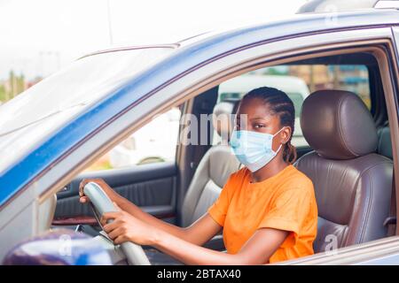 giovane bella donna africana in un veicolo che indossa maschera facciale per prevenire, prevenire, si è impedito dallo scoppio nella società Foto Stock