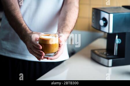 Uomo che tiene cappuccino fatto in casa in una tazza di vetro. Home barista concetto di stile di vita indoor Foto Stock