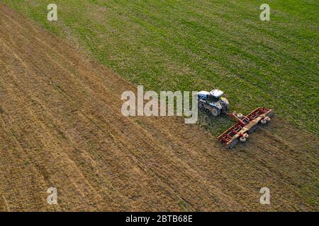 Vista laterale di un aeromobile che sorvola un campo coltivato da un trattore cingolato durante una crisi nel settore agroindustriale 2021. Foto Stock