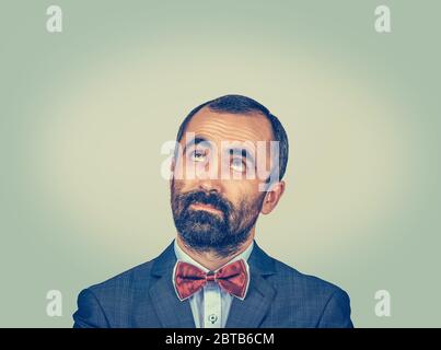 Primo piano ritratto uomo di mezza età guardando in alto. Hipster maschio con barba in abbigliamento formale in studio. Modello bearded misto di razza isolato su verde giallo gradi Foto Stock