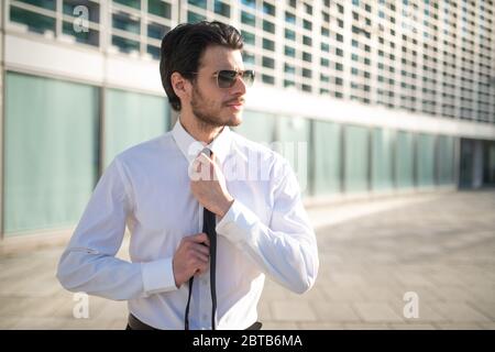 Uomo d'affari che regola la sua cravatta all'aperto in un ambiente di affari moderno, concetto di carriera e di intervista di lavoro Foto Stock