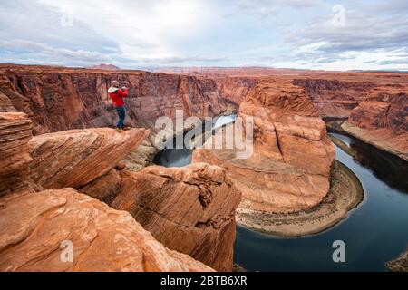 Uomo seduto su una scogliera sul fiume Colorado nel canyon Horseshoe Bend Foto Stock