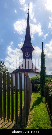 Campanile medievale di una piccola chiesa di villaggio nelle Alpi svizzere tra gli alberi e prati Foto Stock