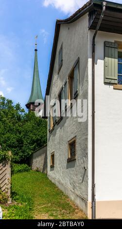 Campanile medievale di una piccola chiesa di villaggio nelle Alpi svizzere tra gli alberi e prati Foto Stock