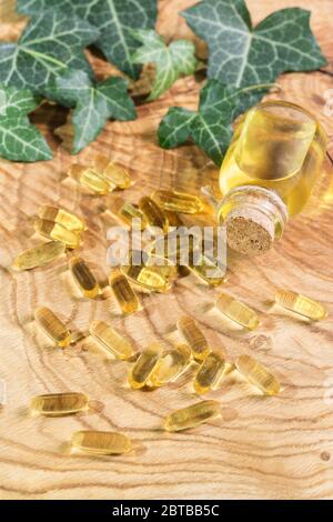 Capsule oblunghe trasparenti di olio di pesce versato sullo sfondo di legno. Acidi grassi polinsaturi Omega-3-essenziali. Olio di semi di lino in una bottiglia. G Foto Stock