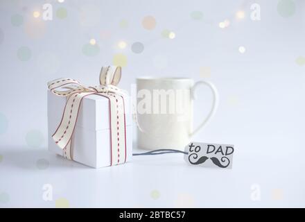 Tazza di caffè del mattino, confezione regalo confezionata, etichetta regalo con parola DAD e icona dei baffi su sfondo chiaro con bokeh Foto Stock