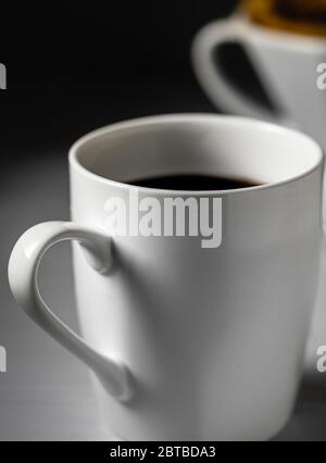 Tazza di caffè con caffè nero e filtro di versamento sullo sfondo. Foto Stock