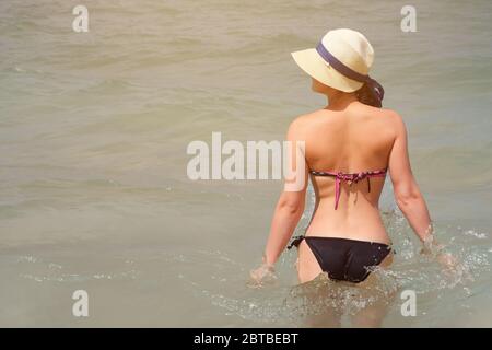 giovane bella donna in bikini e cappello si erge in mare in giornata di sole Foto Stock