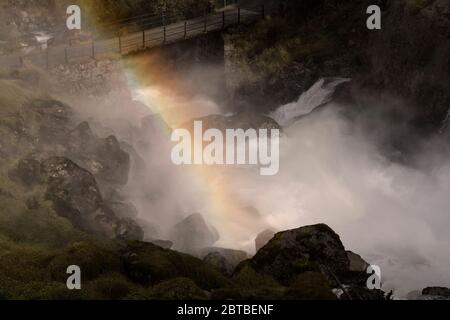 Cascata che attraversa sotto un ponte e l'arcobaleno in una montagna rocciosa sulla strada per il ghiacciaio di Briksdal in Norvegia Foto Stock