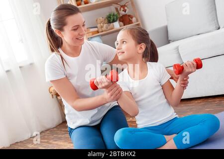 Stile di vita sano. Madre e figlia in abbigliamento sportivo seduto sul tappetino che si esercita con manubri sorridenti gioioso Foto Stock