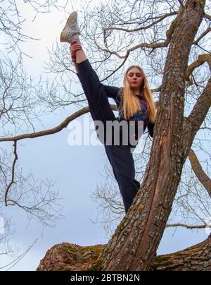 Una ragazza adolescente si leva in piedi su un albero e fa esercizi di stretching. Foto Stock