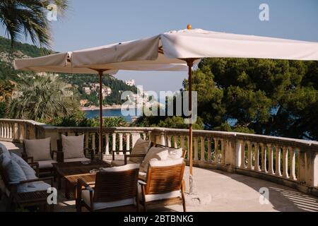 Territorio Villa Shherezade. I migliori hotel in Dubrovnik. Mobili da giardino in legno con cuscini bianchi, sotto un grande ombrello dal sole. Una recinzione Foto Stock