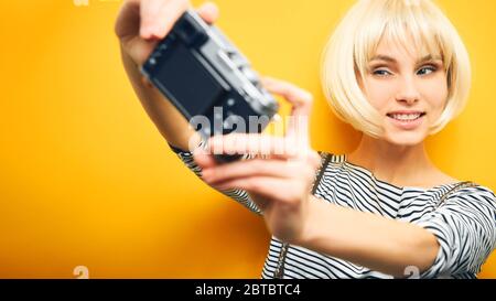 ritratto di una ragazza in un maglione a righe e una parrucca bianca fa un selfie su una macchina fotografica su uno sfondo arancione Foto Stock