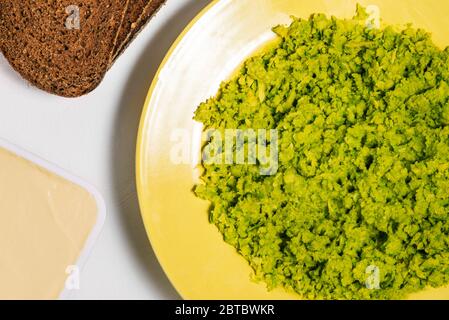 Purè di avocado fresco in un piatto giallo e fette di pane di segale. Il processo di preparazione del toast all'avocado. Cibo sano e dietetico Foto Stock