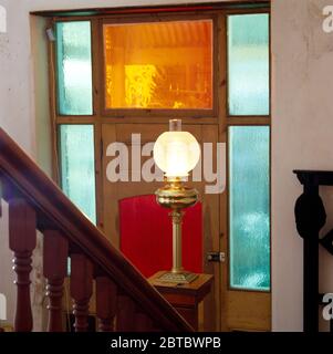 Lampada in vetro e ottone in stile edoardiano su un tavolo davanti ad una porta frontale con pannelli di vetro colorato Foto Stock