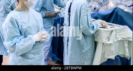 Un chirurgo in maschera medica e in guanti sterili in lattice bianco in sala operatoria. Le dita sono aggrinzate. In background sono medici e medici e Foto Stock