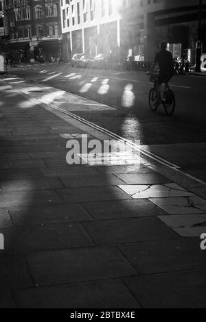 Scena stradale bianca e nera con singolo ciclista che passa sotto il sole Foto Stock