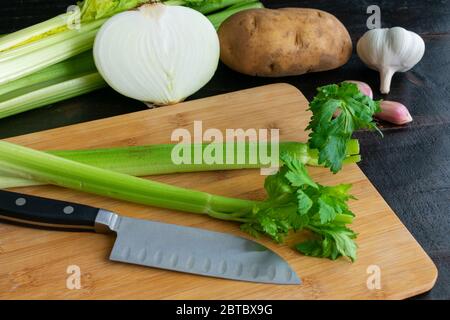 Tritare verdure fresche: Sedano, cipolla, patate e aglio su un tagliere di bambù Foto Stock