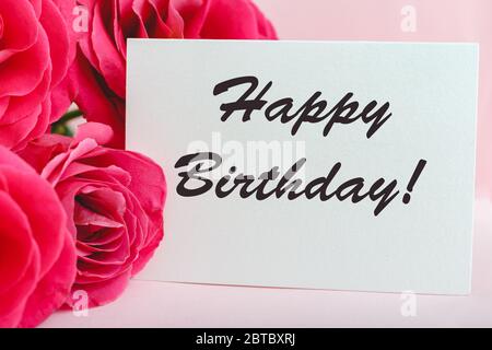 Felice testo di compleanno sulla carta in bouquet di fiori su sfondo rosa. Consegna fiori, carta di congratulazioni. Biglietto d'auguri in rosa rossa Foto Stock