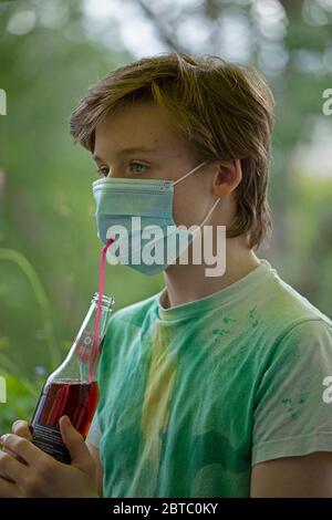 Ragazzo che indossa una maschera di respirazione che beve da una bottiglia usando una paglia, Germania