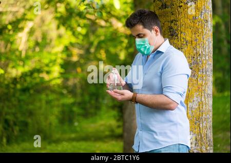 Uomo con maschera protettiva in piedi nel parco, con gel di alcol lavabile a mano, contro la malattia di coronavirus Covid-19 . Concetto antisettico, di igiene e di salute . Foto Stock